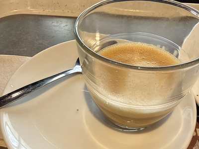 A cortado in a small glass cup on a white saucer with a spoon